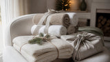 Idées cadeaux linge de maison pour Noël : plaid crème, serviettes de bain roulées et paquet emballé dans un torchon